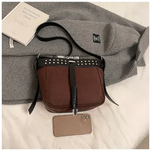 Detail view of brown suede crossbody bag with metal rivets and black leather straps