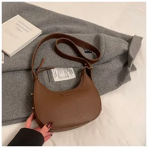 Dettaglio borsa a mezzaluna in pelle marrone con grana su cappotto di lana grigio
