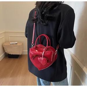 Borsa rossa a forma di cuore con fiocco indossata da modella in completo nero