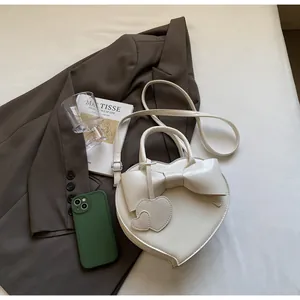 Dettaglio ravvicinato di una borsa bianca a forma di cuore con fiocco decorativo e ciondoli