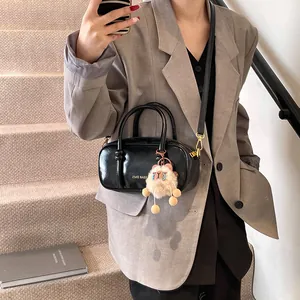 Glossy black mini crossbody bag with plush charm shown in a minimalist outdoor setting