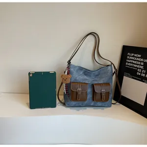 Detail of blue denim tote bag with brown leather pockets and a small plush bear charm