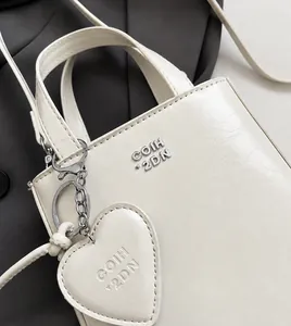 Detail of cream crossbody bag with wrinkled texture, metal logo and heart charm
