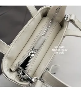 Detail of a smooth silver metal zipper and fine stitching on a creamy white handbag
