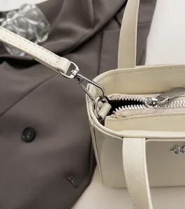 Close-up of silver metal buckles and textured leather on a cream crossbody bag