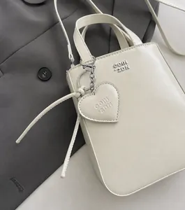 Close-up of cream mini leather handbag with GOIH 2DN logo and heart-shaped charm on grey blazer