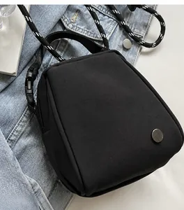 Detail of black mini crossbody shell bag with braided rope strap on denim fabric