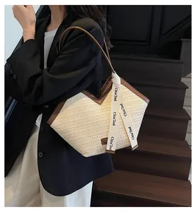 Detail of woven straw tote bag with brown leather trim and decorative brand ribbon