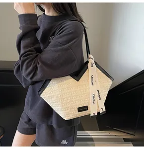 Detail of cream straw tote bag with black leather straps and hanging letter ribbon