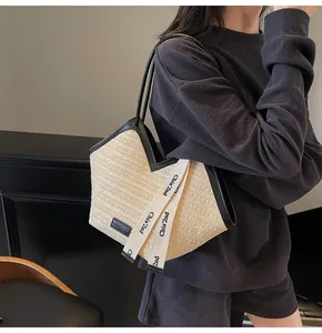 Detail of straw tote bag with V-shaped opening, black leather trim and white ribbon charm