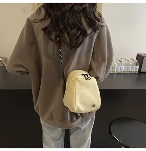 Detail of off-white shell-shaped crossbody bag with striped strap on a model