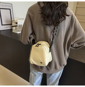 Detail of beige nylon shell bag with striped rope strap shown on a model