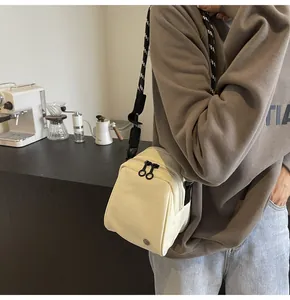 Detail of off-white shell crossbody bag with adjustable woven strap and dual zippers