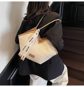 Detail of a beige woven tote bag featuring brown leather trim and a white logo ribbon