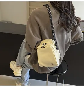 Detail of a cream rectangular crossbody bag with dual ring zippers and rope shoulder strap