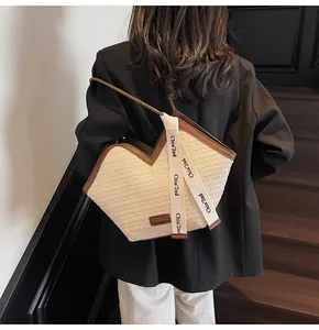 Detail of beige woven tote bag with brown leather trim and decorative side strap