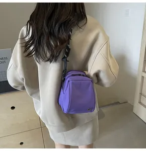 Detail of purple crossbody bag with adjustable striped strap shown on a model