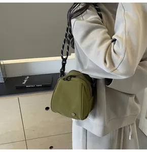 Olive green mini crossbody bag with black and white rope strap worn on a grey outfit