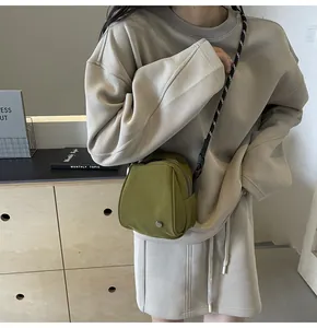 Detailed side view of an olive green crossbody shell bag with a striped woven strap