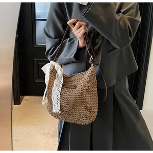 Detail of hand-woven straw crossbody bag featuring a large white lace bow and leather strap