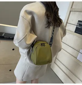 Detail shot of an olive green canvas crossbody bag worn by a model in a minimalist room