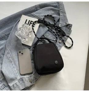 Close-up of black crossbody bag with woven rope strap and silver hardware on denim jacket