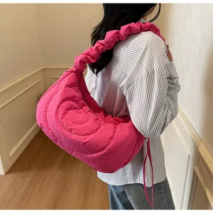 Close-up of rose pink quilted shoulder bag with heart pattern and pleated strap detail