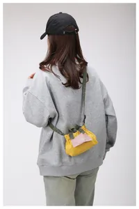 Dettaglio di una borsa mini in tela giallo acceso con spalline verde oliva su una modella