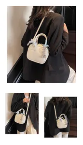 Detail of cream mini bowling bag with heart stitching, lace bow, and silver bear charm