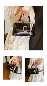 Detail of black glossy handbag with silver square buckle and woven key charm accessory