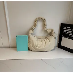 Detail of beige quilted dumpling bag with spiral texture and ruched strap showing size scale