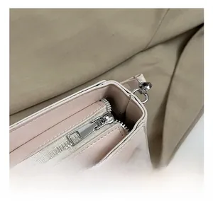 Close-up of smooth metal zipper and silver hardware on a textured beige handbag