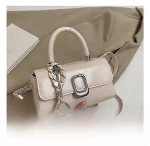 Detail of a beige-pink square crossbody bag with metallic clasp and decorative charms