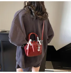 Detail view of red patent leather mini bowling bag with decorative bow and heart charm