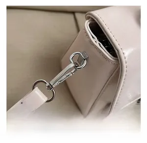 Close-up of silver metal lobster clasp and stitched leather strap on a beige handbag