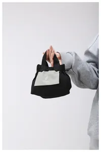 Dettaglio ravvicinato di una mini borsa tote in tela nera con logo del sole e manico