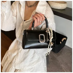 Detail of black glossy handbag featuring silver buckle and side hanging charm ornaments