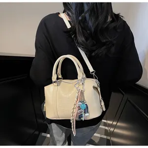 Close-up of beige bowling bag with letter embossing and decorative charm on shoulder strap