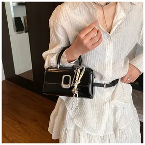 Detail of black glossy handbag featuring a silver square twist lock and woven charm