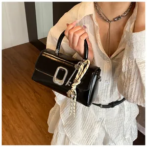Detailed view of black patent leather crossbody bag with silver buckle and braided charm