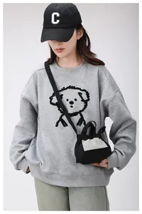 Dettaglio di una mini borsa a tracolla nera con logo su una felpa grigia sportiva