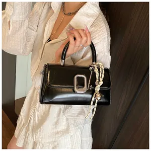 Detail of black glossy handbag featuring silver buckle and woven bell charm accessory