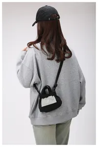 Dettaglio di una piccola borsa a tracolla in tela nera con patch logo indossata da modella