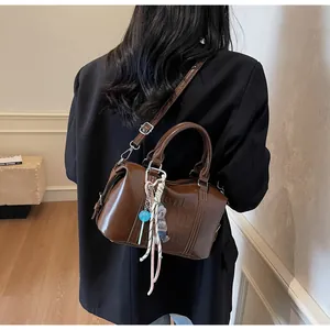 Brown gloss Boston bag with adjustable strap and bear charm shown worn over the shoulder