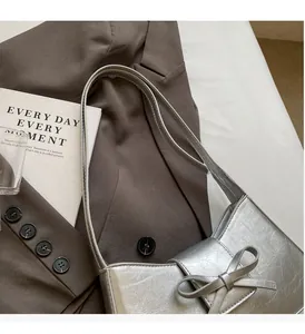 Silver crescent underarm bag with pleated texture and bow detail on brown suit background