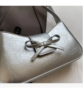 Close-up of silver underarm bag with metallic texture, pleats and a minimalist bow detail
