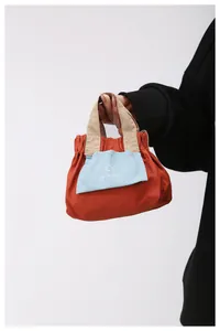 Dettaglio mini borsa a tracolla arancione con tasca blu e manici superiori kaki