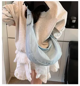 Détail d'un sac hobo en jean bleu clair porté par un modèle au design croissant