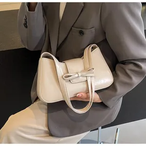Detail of a creamy white PU leather handbag with a 3D bow decoration and slim handles