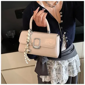 Detail of cream patent leather handbag featuring silver buckle and woven rope charm